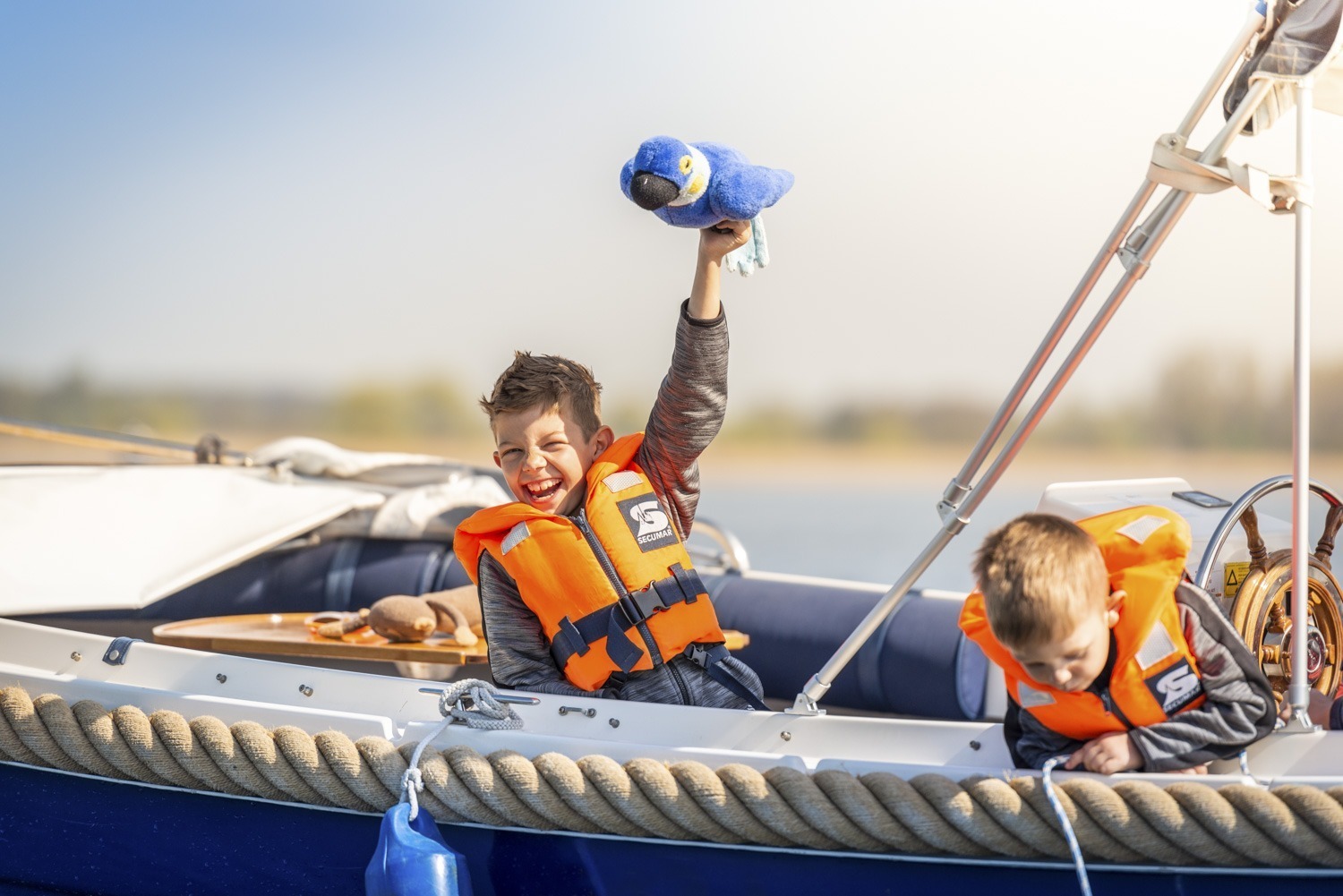 Zwei kleine Jungs haben Spaß auf einem Boot in der Havel in Werder. Einer lässt einen Stoffpapagei fliegen, der andere hat ein Seil ins Wasser getaucht und schaut daran hinunter.